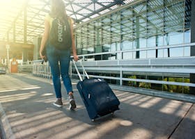 A woman walks with a suitcase outside an airport terminal, ready for travel.