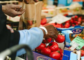 Close-up of elderly hands selecting ripe tomatoes at an outdoor vegetable market.